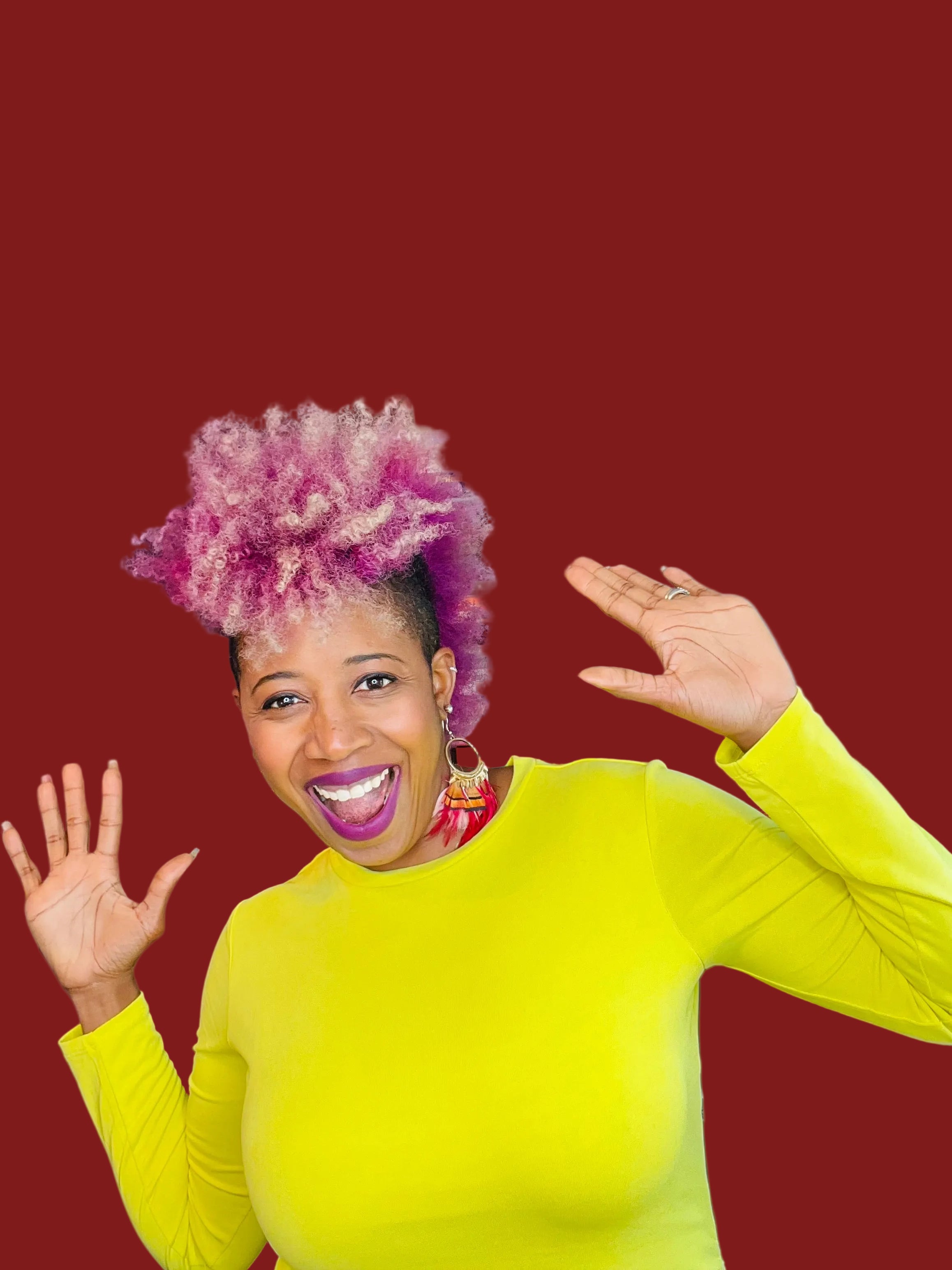 Person with pink hair and a yellow sweater in front of a bookshelf