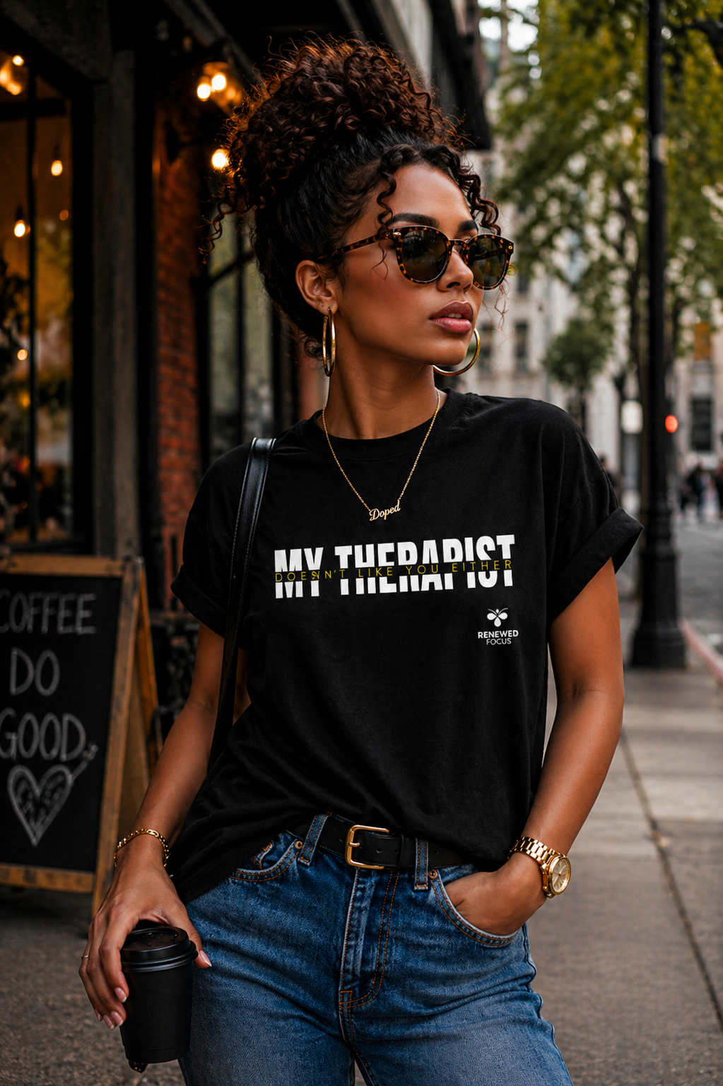 Woman wearing a black t-shirt with text, sunglasses, and carrying a coffee cup on a city street.